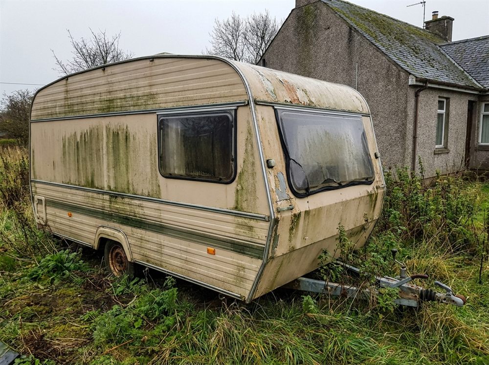Old caravan with heavy green algae staining and a cracked window seal
