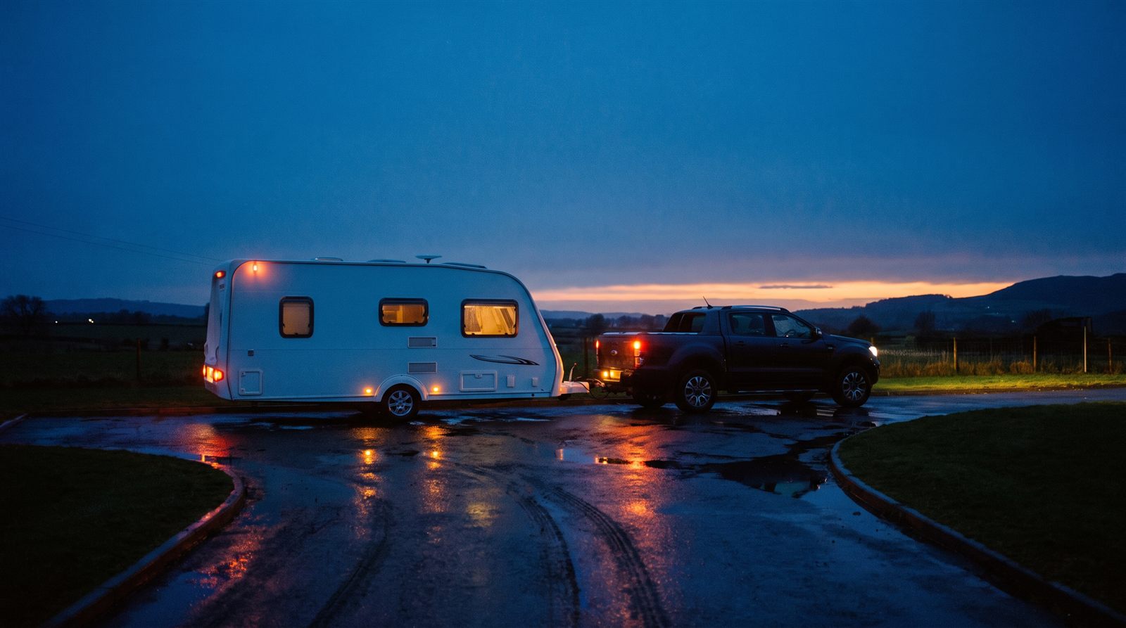 Touring caravan hitched to a pickup truck at dusk, ready to be collected